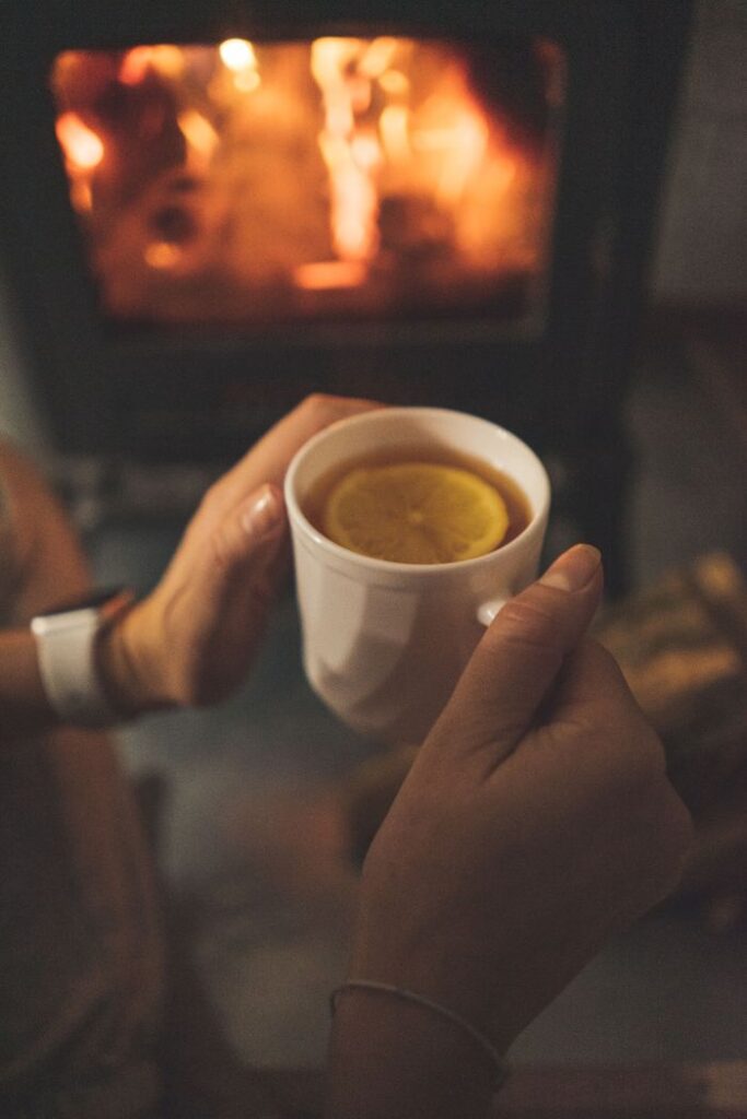 pexels photo 12932890 Close-up of hands holding lemon tea mug by a fireplace, offering warmth and comfort.
